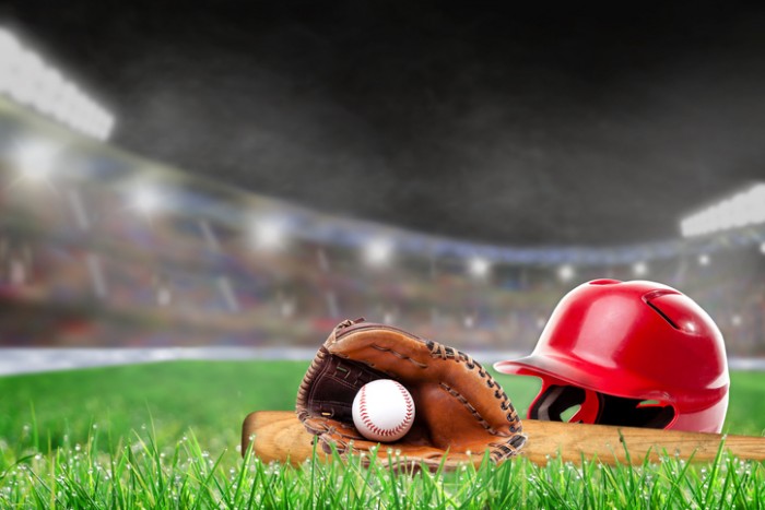 Baseball helmet, bat, glove and ball on grass in brightly lit outdoor stadium. Focus on foreground and shallow depth of field on background with copy space. Fictitious background stadium created entirely in Photoshop.